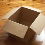 Emptied cardboard box with the flaps open standing on a wooden parquet floor conceptual of packaging, mail, storage, or removals
