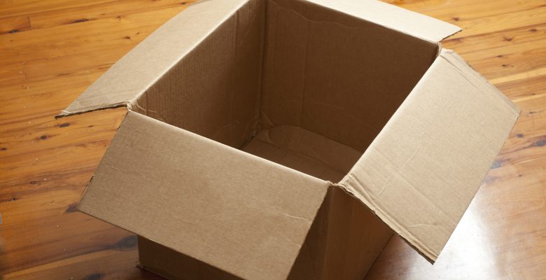 Emptied cardboard box with the flaps open standing on a wooden parquet floor conceptual of packaging, mail, storage, or removals